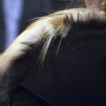 A woman in a black coat with a fur collar stands facing away from the camera